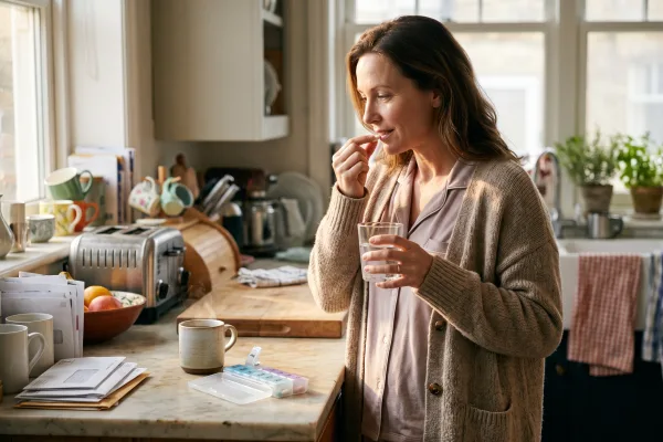 Woman taking a daily thyroid pill with a glass of water in her kitchen in the morning